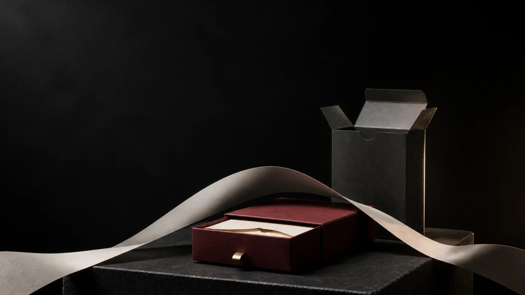 Illustrative Tidal Precision scene with an oxblood drawer box, graphite carton and sweeping ivory paper ribbon on a dark plinth