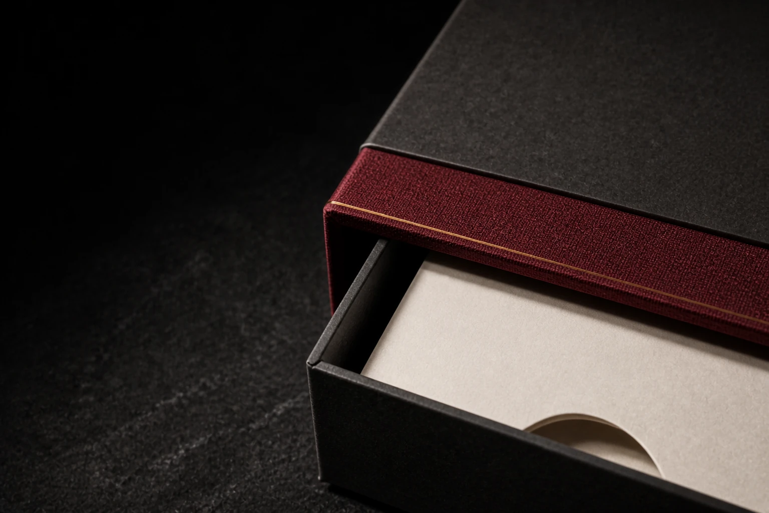 Macro illustrative study of a graphite drawer box, oxblood woven wrap, ivory insert aperture and fine brass edge