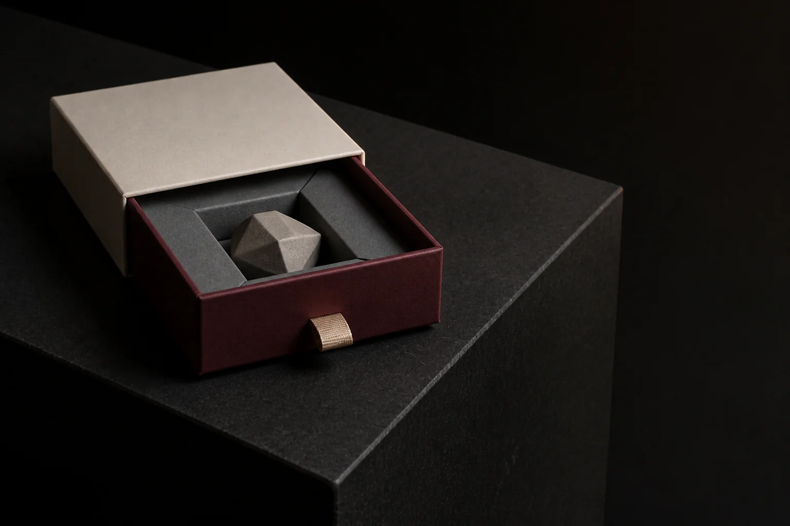 Illustrative open ivory-and-oxblood drawer box with a graphite insert and abstract stone form